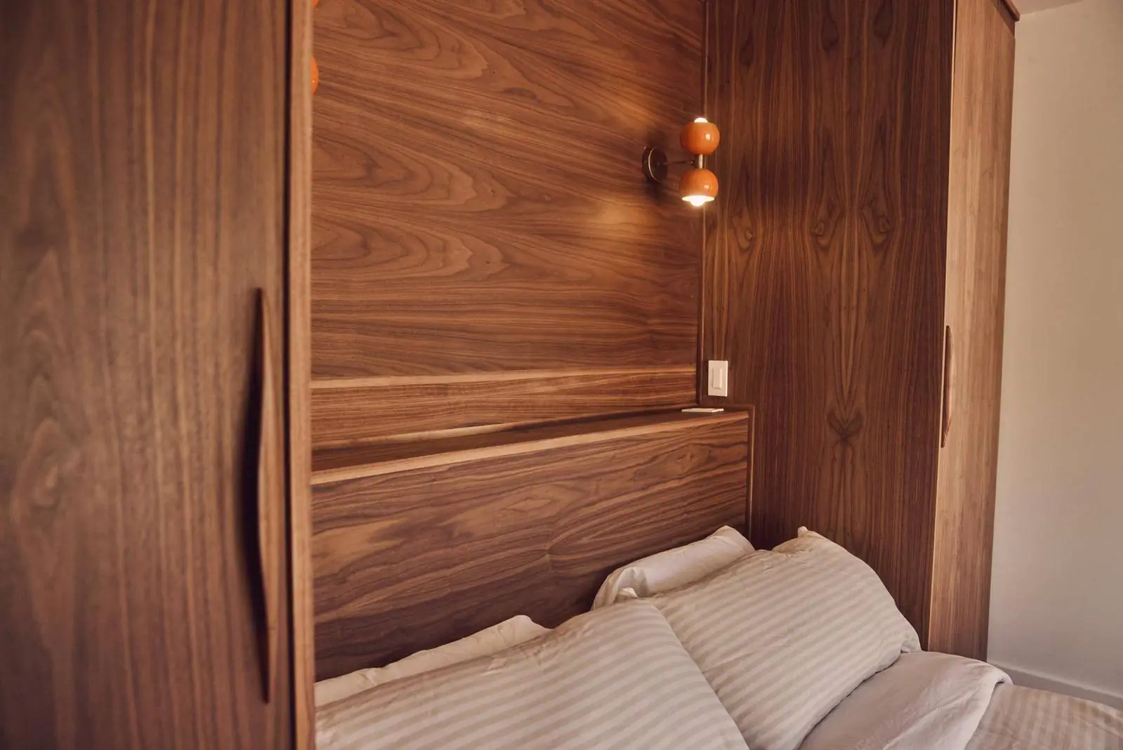 Walnut-paneled wall with brass sconces over the bed, Ojai East End