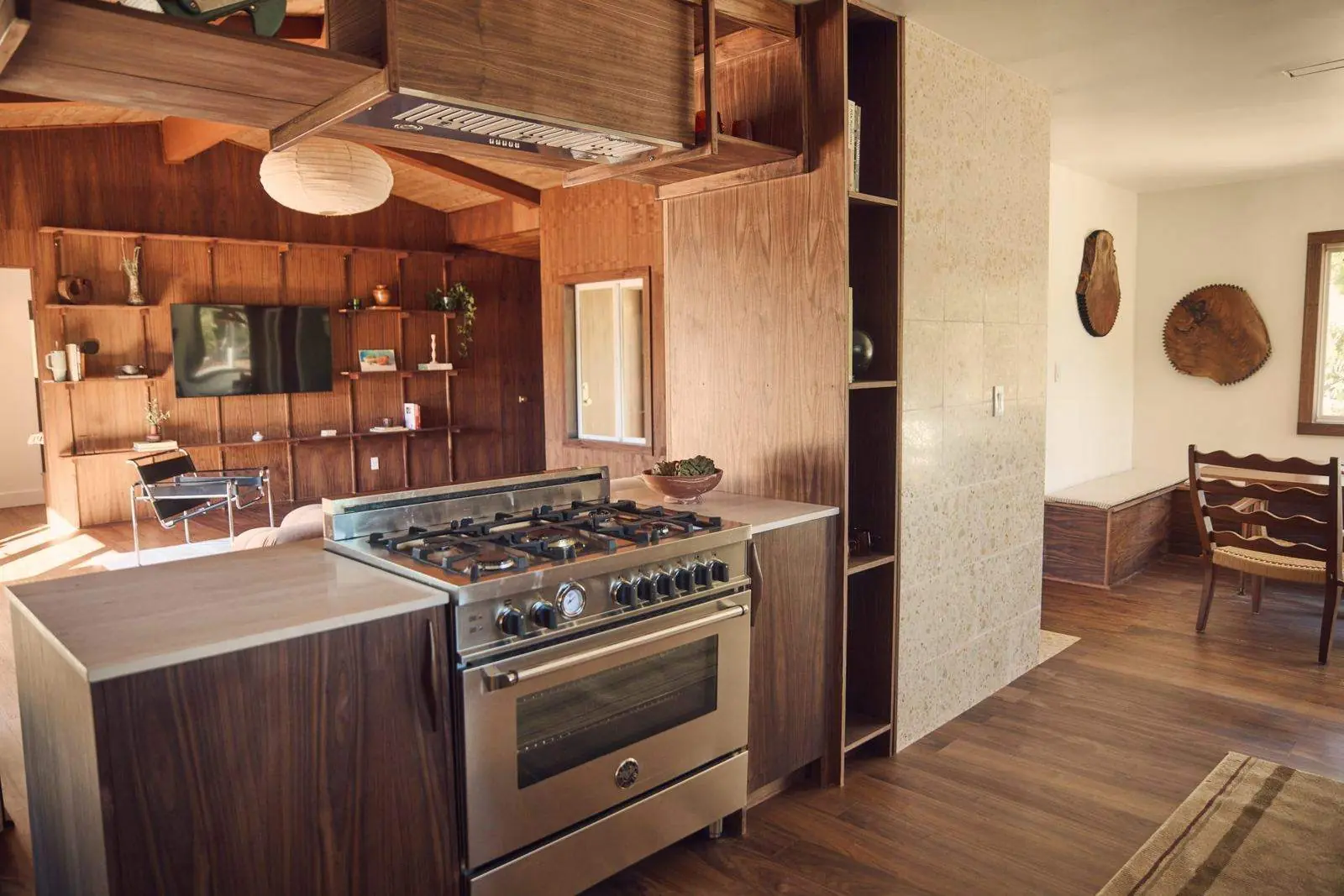 A walnut-paneled kitchen with a range and open shelving